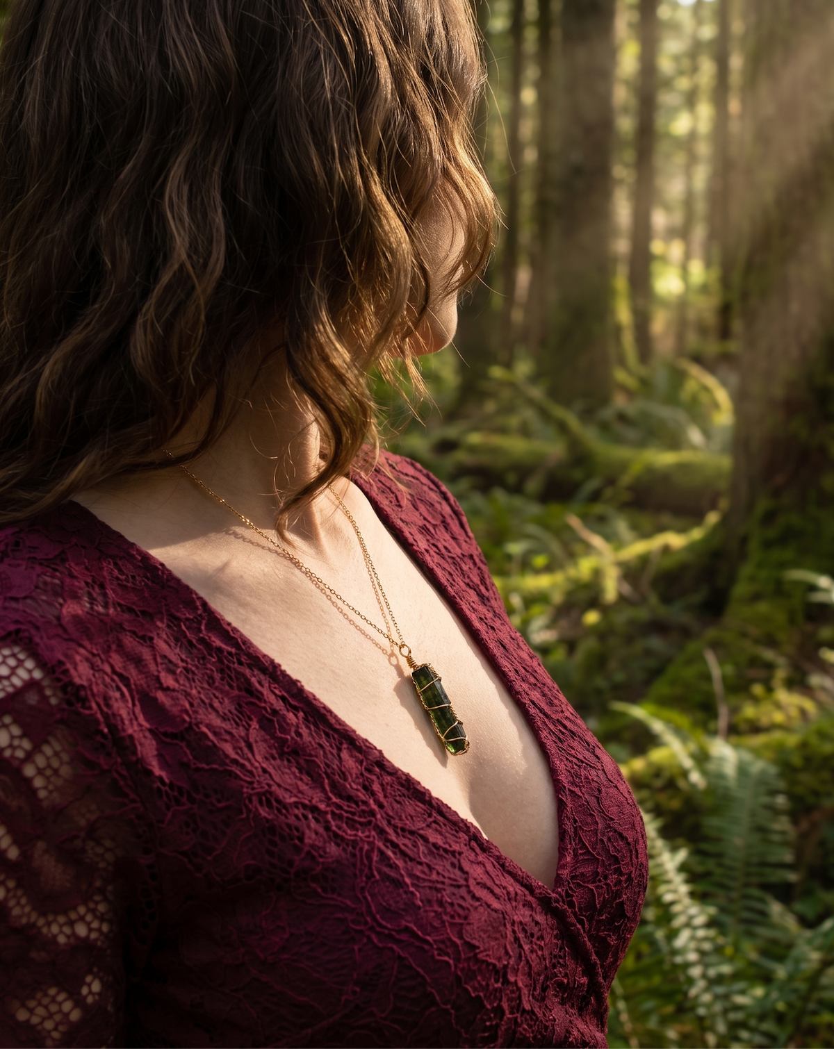 Raw emerald pendant wrapped in gold-tone wire on a gold-tone chain, worn at the collarbone